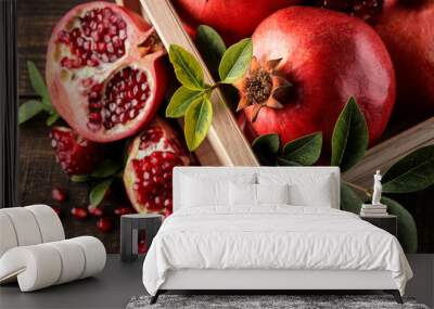 Ripe tasty red pomegranate fruit with leaves in a wooden box on a brown wooden table. top view Wall mural