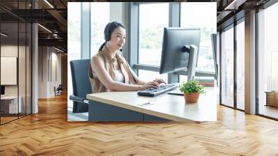 Attractive and smile young asian customer servicer woman wearing headset in modern creative meeting working office look at computer monitor,work from and social distancing concept. Wall mural