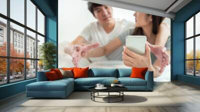 Secretly listening to conversation over phone or peeping social posts, messages.Asian young man and woman fight over on smart mobile phone with argument relationship concept Wall mural