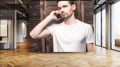 Handsome businessman in white t-shir talking on the smartphone. A young man looks like an executive director or head of a company or enterprise. Room in loft style. Wall mural