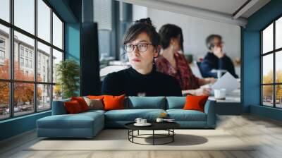 Portrait of  confident businesswoman working on computer in creative office. Coworkers in the background. Wall mural