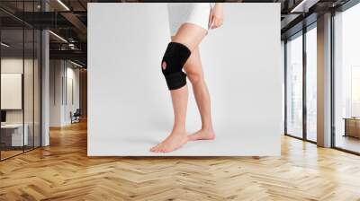 Knee Support Brace on leg isolated on white background. Elastic orthopedic orthosis. Anatomic braces for knee fixation, injuries and pain. Protective knee joint bandage sleeve. Trauma, rehabilitation Wall mural