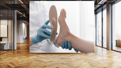 Orthopedic insole on a white background. Hands in rubber gloves hold an orthopedic insole. Foot care, comfort for the feet. Doctor orthopedist tests the medical device. Flat feet correction Wall mural