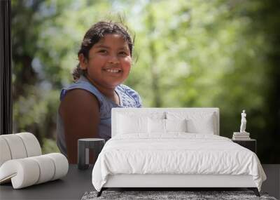 A young latino girl with a smile who is enjoying natures beauty, surrounded by trees with green foliage. Wall mural