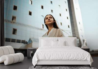 against the background of a building made of glass and concrete, a girl stands dreamily looking into the distance Wall mural