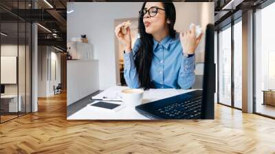 woman is sitting at the table in the office and eating a sandwich Wall mural