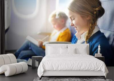 Adorable little children traveling by an airplane. Girl sitting by aircraft window and reading her ebook during the flight. Wall mural