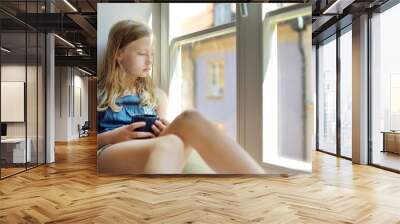 Beautiful preteen girl looking out the window. Young girl sitting on a windowsill. Wall mural