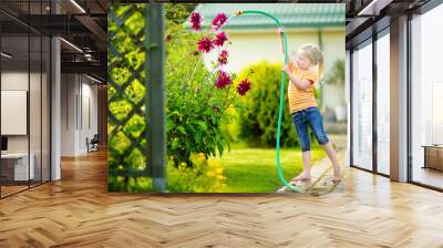 Cute little girl watering flowers in the garden at summer day. Wall mural