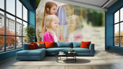 Cute little girls watching animals at the zoo on warm and sunny summer day. Children watching zoo animals through the window. Wall mural