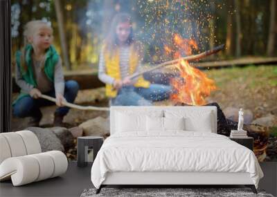 Cute little sisters roasting hotdogs on sticks at bonfire. Children having fun at camp fire. Camping with kids in fall forest. Wall mural