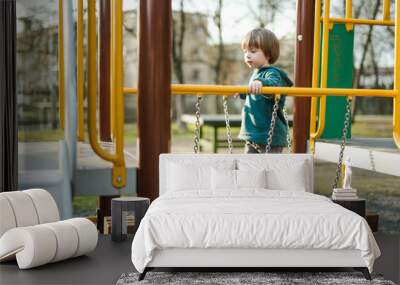 Cute toddler boy having fun on a playground outdoors on warm summer day. Active leisure for kids. Wall mural