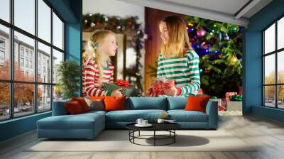 Happy little sisters wearing Christmas pajamas opening gift boxes by a fireplace in a cozy dark living room on Christmas eve. Wall mural