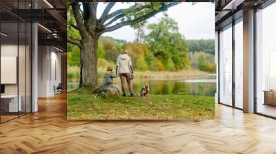 Mother and her little son walking their pedigreed Australian terrier dog in late autumn park. Fall portrait of black and sable tan purebred Australian terrier. Wall mural