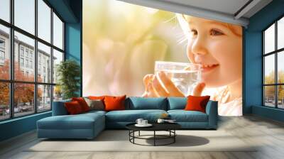 Pretty little child drinking fresh water on sunny summer day at home. Cute preschool kid holding glass of pure mineral water. Healthy lifestyle for kids. Wall mural