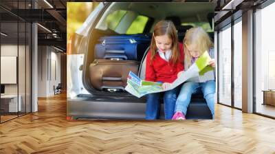 Two adorable little girls ready to go on vacations with their parents. Kids sitting in a car examining a map. Wall mural