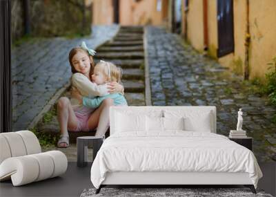 Two adorable little sisters laughing and hugging each other on warm and sunny summer day Wall mural