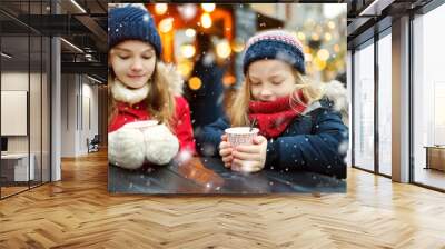 Two adorable sisters drinking hot chocolate on traditional Christmas fair in Riga, Latvia. Children enjoying sweets, candies and gingerbread on Xmas market. Wall mural