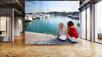 Two cute little sisters watching small yachts in harbor in Desenzano del Garda on beautiful autumn day Wall mural