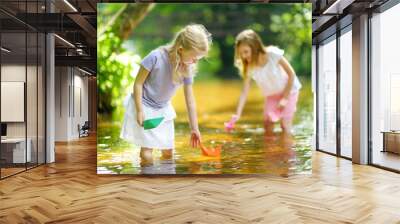 Two little sisters playing with paper boats by a river on warm and sunny summer day. Children having fun by the water. Wall mural