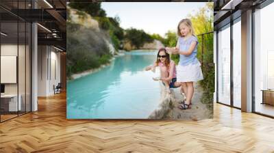 Two young sisters playing by natural swimming pool in Bagno Vignoni, with thermal spring water and waterfall. Tuscany, Italy. Wall mural