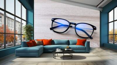 Pair of classic black reading glasses on wooden table. Glasses with filter coating blocking screen's blue light to prevent computer vision syndrome (CVS) or digital eye strain. Wall mural