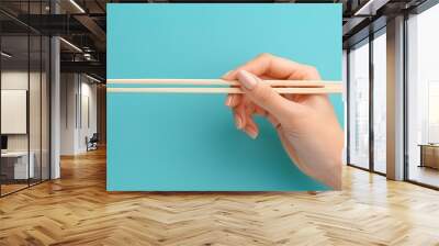 A hand holding wooden chopsticks isolated on a plain background  Wall mural