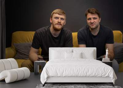 two cheerful handsome guys play passionately video game holding console joystick in hands. emotionally clicking control buttons on comfy sofa Resting At Home. Crazy Male gamers Couple gaming concept Wall mural