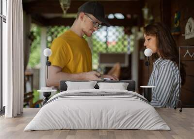 uniformed delivery man handing paper bags of food to Attractive smiling girl. young woman using smartphone to pay for her order. new online payment technologies concept Wall mural