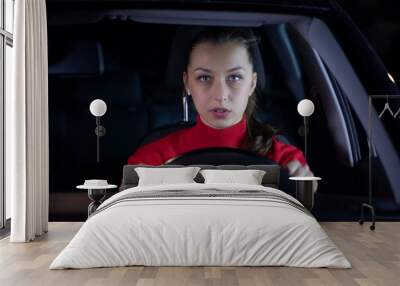 Woman is driving car at night. Serious female driver sitting inside car looks confused forward to the road clings tight to wheel on night trip. Concept: nerves and transportation. Safe journey Wall mural