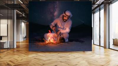 Arab young man sitting around bonfire in the desert, Arabic comping, middle east tourism concept. Wall mural