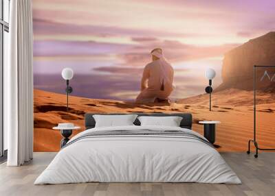 Arabic man with traditional emirates clothes sitting on kness in the UAE desert. Sunset time. Wall mural