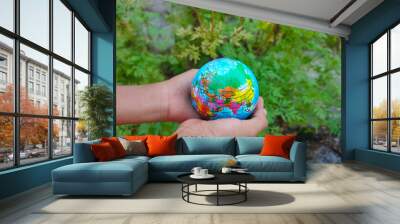 A child’s hand holds an earth globe with a green nature background. The concept of the future of the earth and children. Wall mural