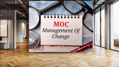 Magnifying glass,glasses,compass,pen and notebook with text MOC Management of Change on a wooden background. Wall mural