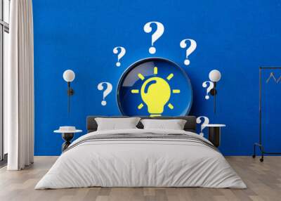 Problem solving concept.Magnifying glass focus on light bulb icon among question mark icon on blue backgroud Wall mural