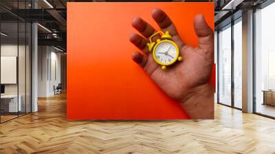 Yellow alarm clock in the palm of someone's hand on an orange background Wall mural