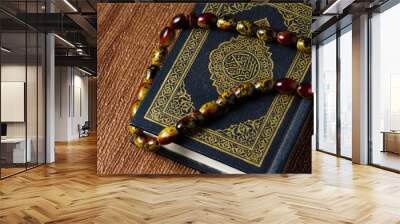 The Quran with rosary beads or “tasbih” and compass on wooden surface. Arabic characters means : Holy Quran, the Holy book of Islam. Islamic concept. Wall mural