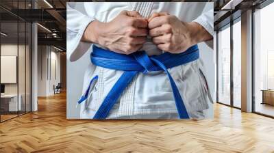 Man in White Judo Kimono Tying Blue Belt Close-Up on White Background Wall mural