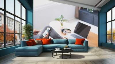 Young attractive man sitting on sofa using smart phone at home. Wall mural