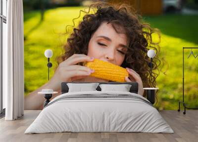 a beautiful girl eats delicious corn against a background of green grass. curly girl eats corn. Wall mural