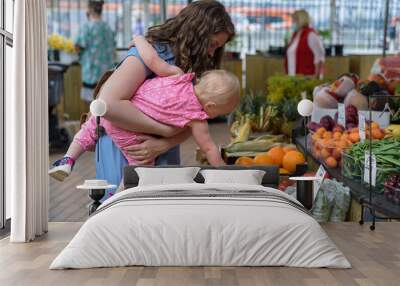 Woman buying vegetables with baby girl on farmers food market Wall mural