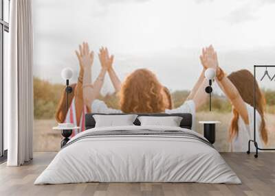 Boho women sitting in circle with arms raised connected in rural field Wall mural