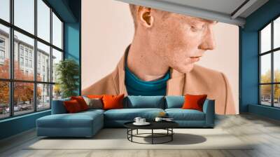 Close-up portrait of young man with red hair and freckles. Dressed in turquoise throat sweater and brown coat. Studio shot Wall mural