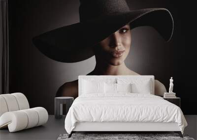 Dark studio portrait of elegant sexy woman in black wide hat and black dress. Wall mural