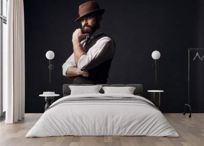 Low key portrait of attractive serious man with dark hair, mustache and beard in white shirt, brown vest and colorful striped tie. Hand near face. Studio shot. Wall mural