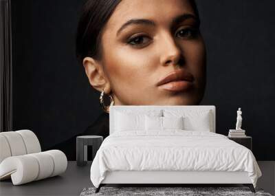 portrait of a dark-eyed beautiful girl with professional make-up, dressed in a black jacket, she has gold earrings and looks at camera Wall mural