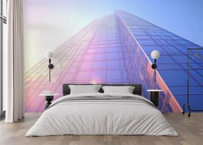 Modern glass skyscraper under a clear blue sky, morning sunlight reflecting off sleek surfaces, showcasing contemporary architecture and urban design. Wall mural