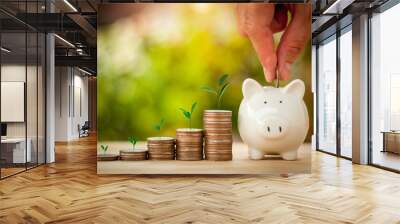 Hand putting coins in a piggy bank for save money with sun light bokeh background and tree growing on coin. Saving Money concept. Wall mural