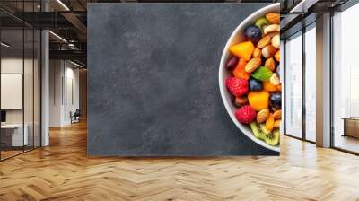 Vibrant fruit and nut medley, a colorful display of fresh berries, mango, kiwi, and various nuts, served in a white bowl against a dark textured backdrop. Wall mural