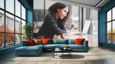 A cheerful young woman is working on her laptop in a bright, modern coffee shop, exuding productivity and contentment. Wall mural